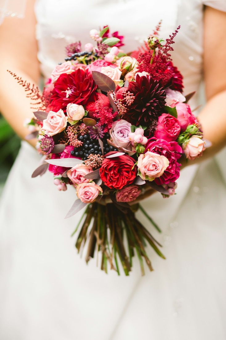 A bride holding a red and pink bouquet
